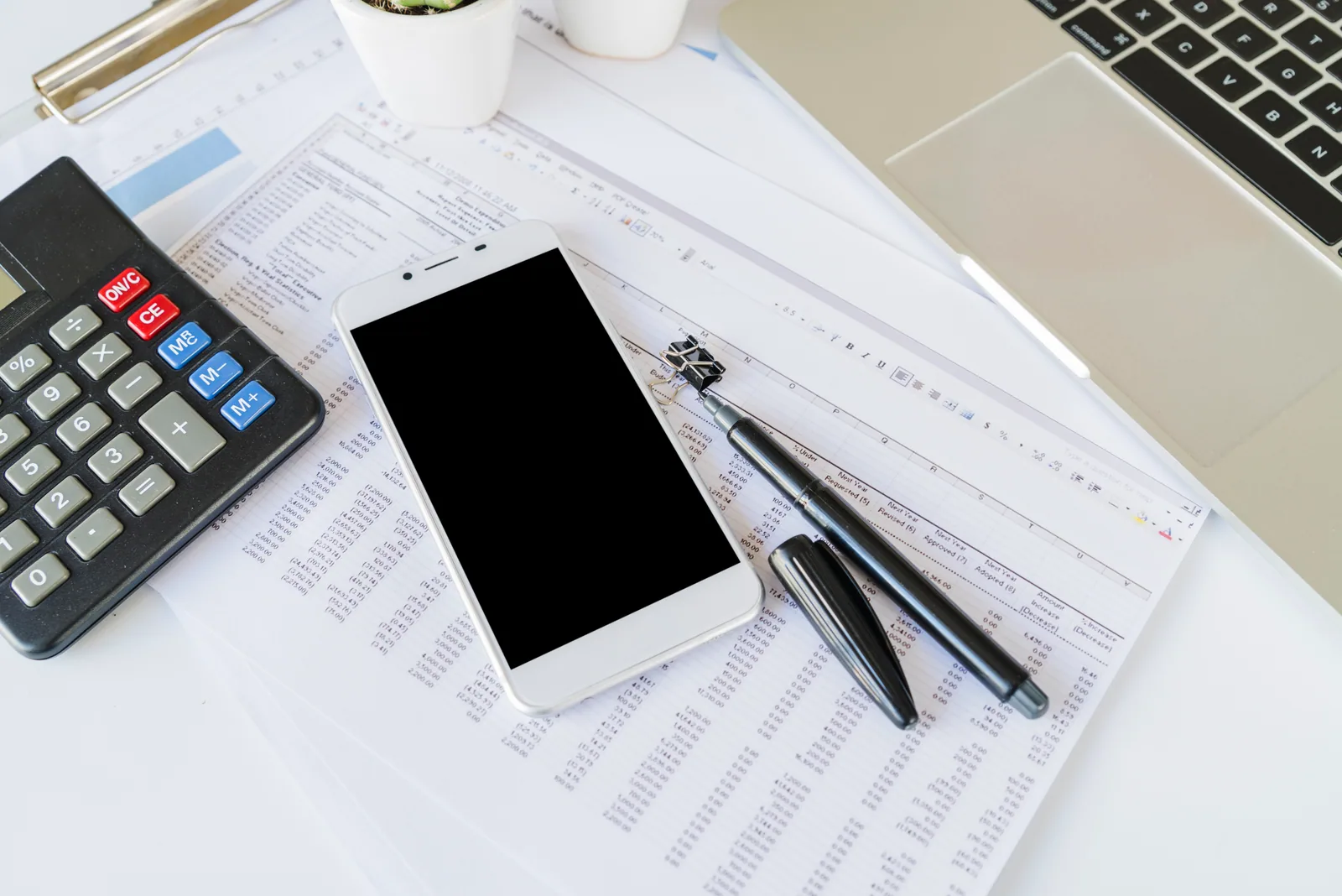 KVKK danışmanlık ücreti ve maliyet hesabı Rakam tablolarının üzerinde hesap makinesi, akıllı telefon ve kalem; KVKK danışmanlık ücretini belirleyen maliyet hesabını anlatıyor