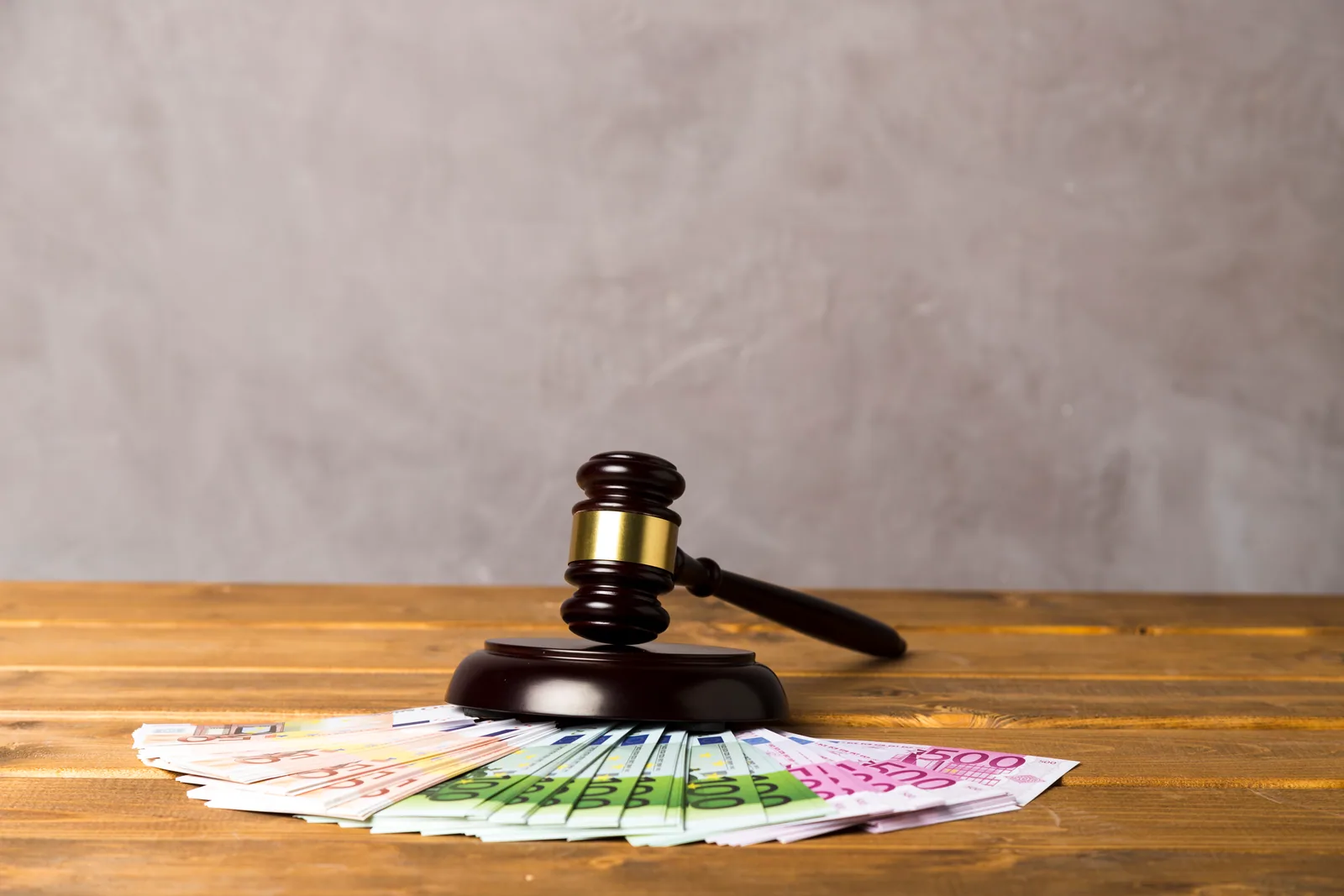 Ahşap masada hâkim tokmağı ve önünde yelpaze biçiminde dizilmiş avro banknotlar; idari para cezası kavramını anlatıyor