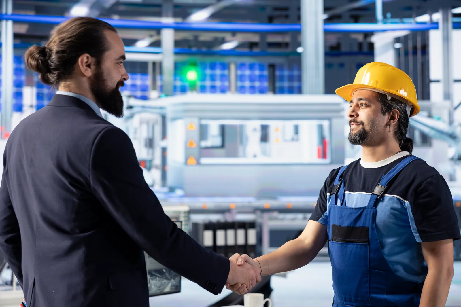 Fabrika içinde takım elbiseli yönetici ile baretli işçinin el sıkışması; asıl işveren ile alt işveren arasındaki iş ilişkisini simgeliyor