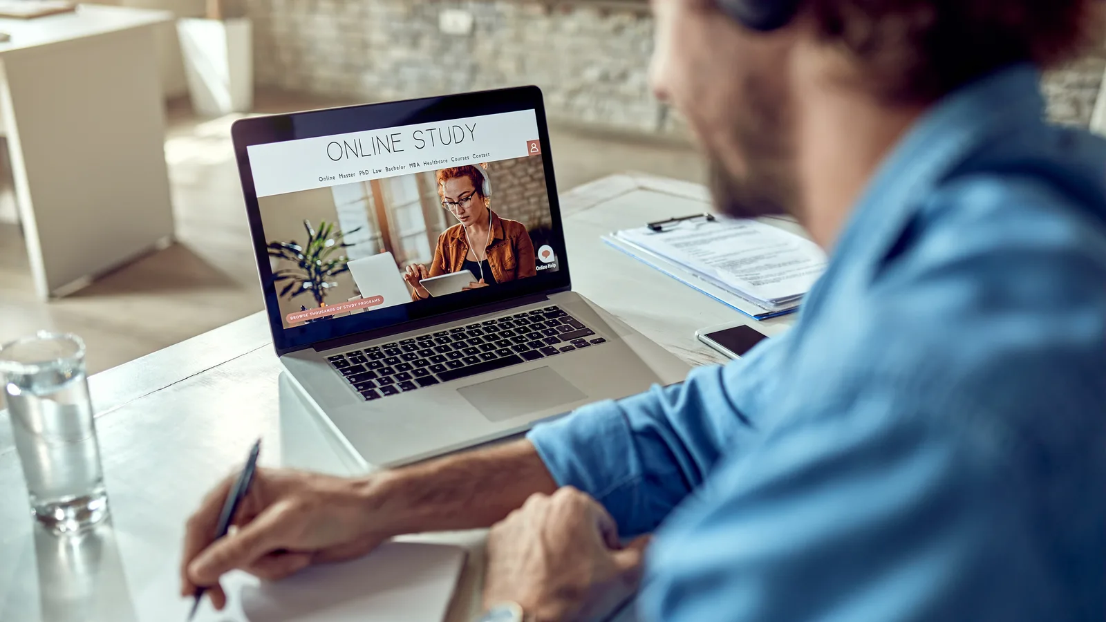 Ofisinde bilgisayarı başında oturan çalışan, ekrandaki online KVKK farkındalık eğitimi videosunu izleyip not alıyor